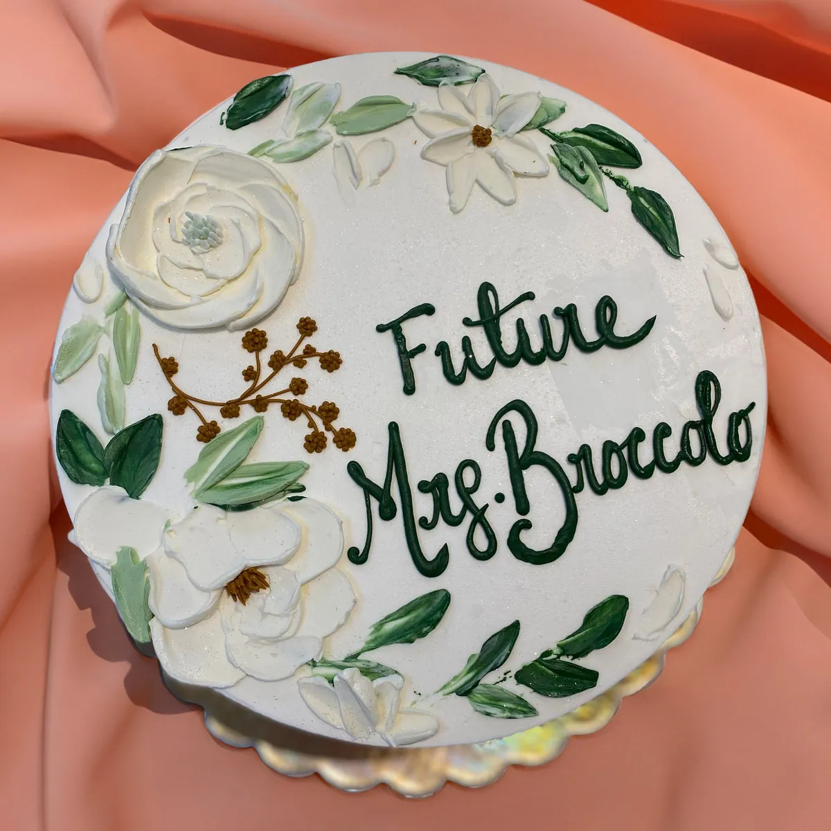 Round cake with painted white flowers and green script lettering