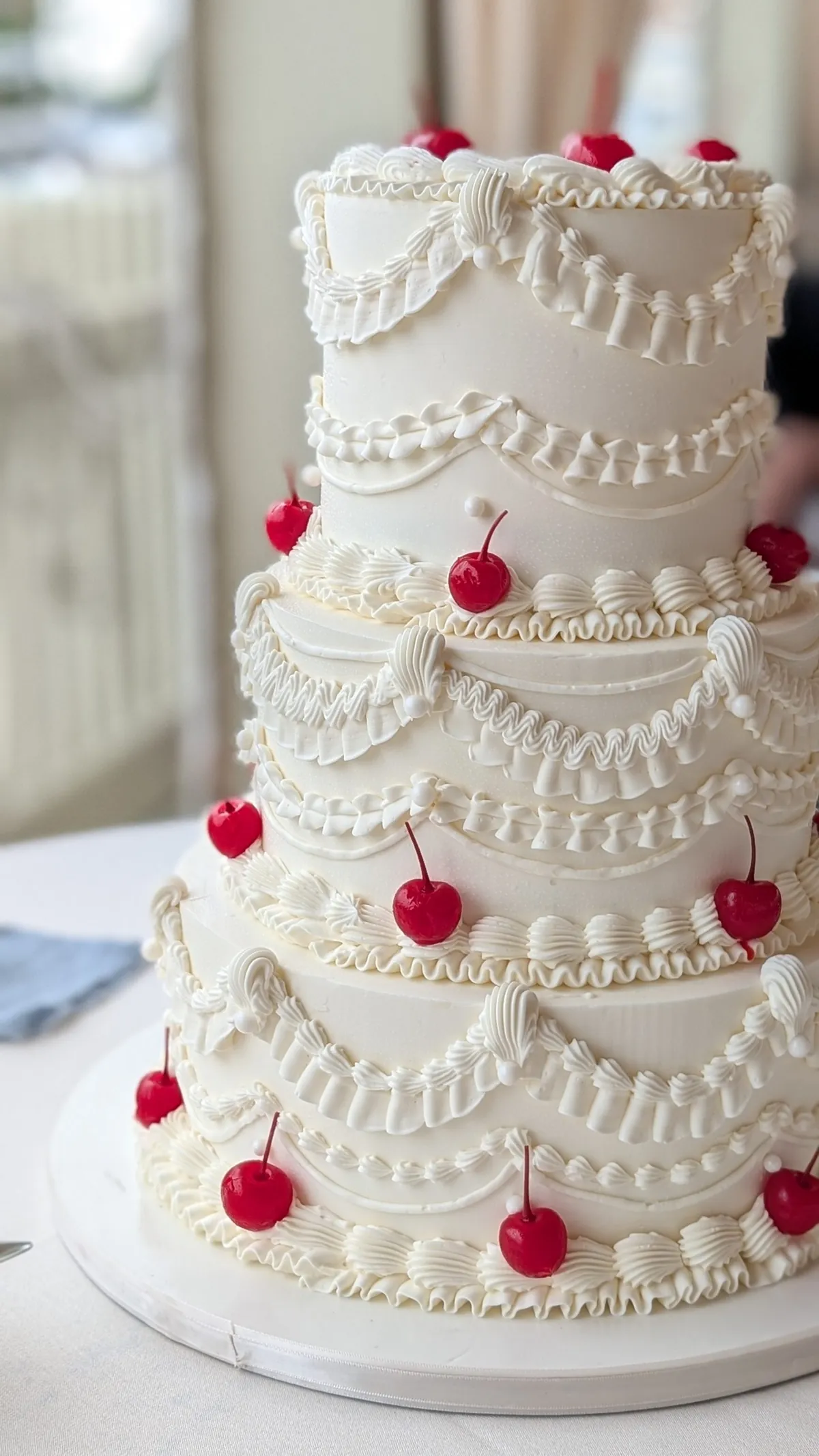 Three-tier white buttercream wedding cake with vintage swags and red cherries